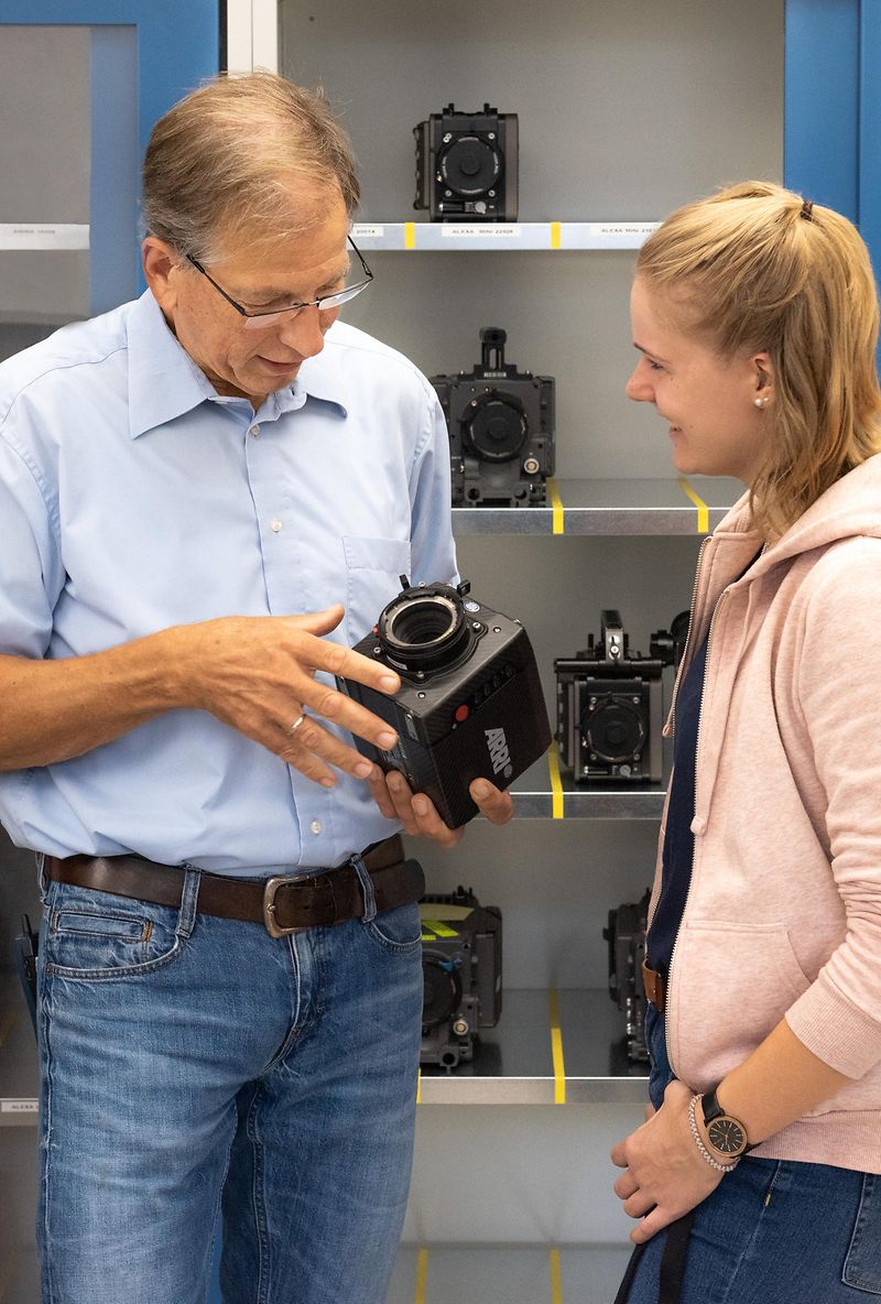 A man explains something about alexa 35 in his hand with a girl standing next to him