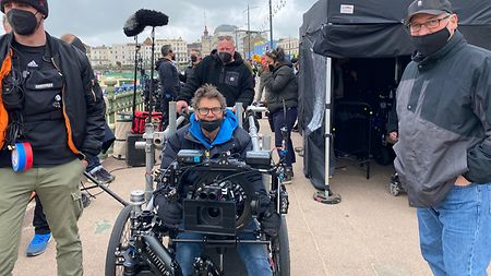Key grip Gary Hymns seated in a rickshaw dolly, holding MAXIMA supported by Steadicam arm.